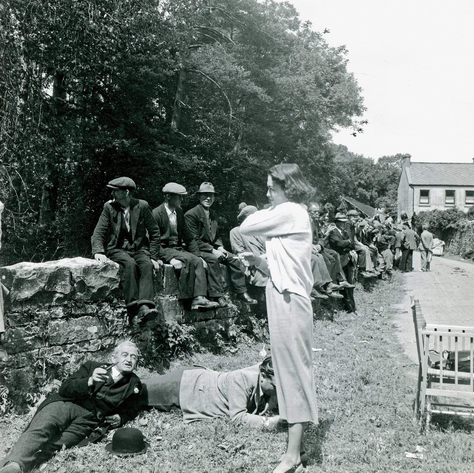 Cast and crew relaxing between takes during the filming of The Quiet Man. Actor Barry Fitzgerald is lying on the ground on the bottom left, Ernie is standing in background on the road, County Mayo, 1951.