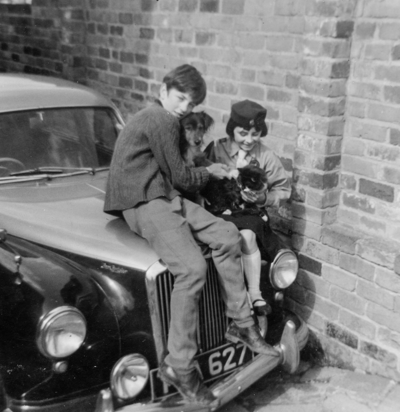 Meehaul and Fionnghuala Smith sitting on a car with family dog Whiskey, Birmingham c. 1967.